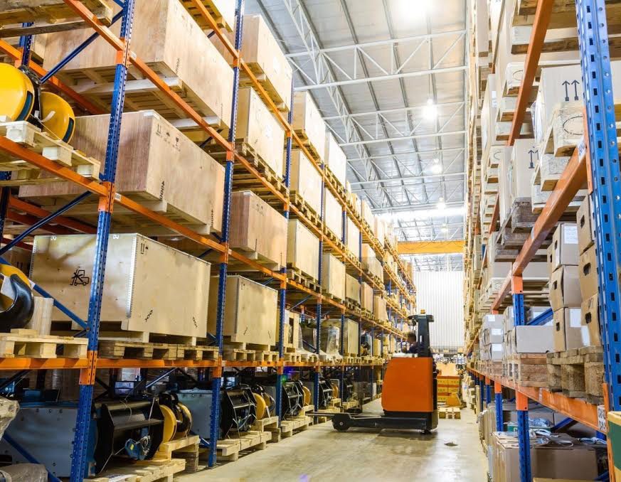 Racked warehouse aisle with crated cargo and a forklift in operation